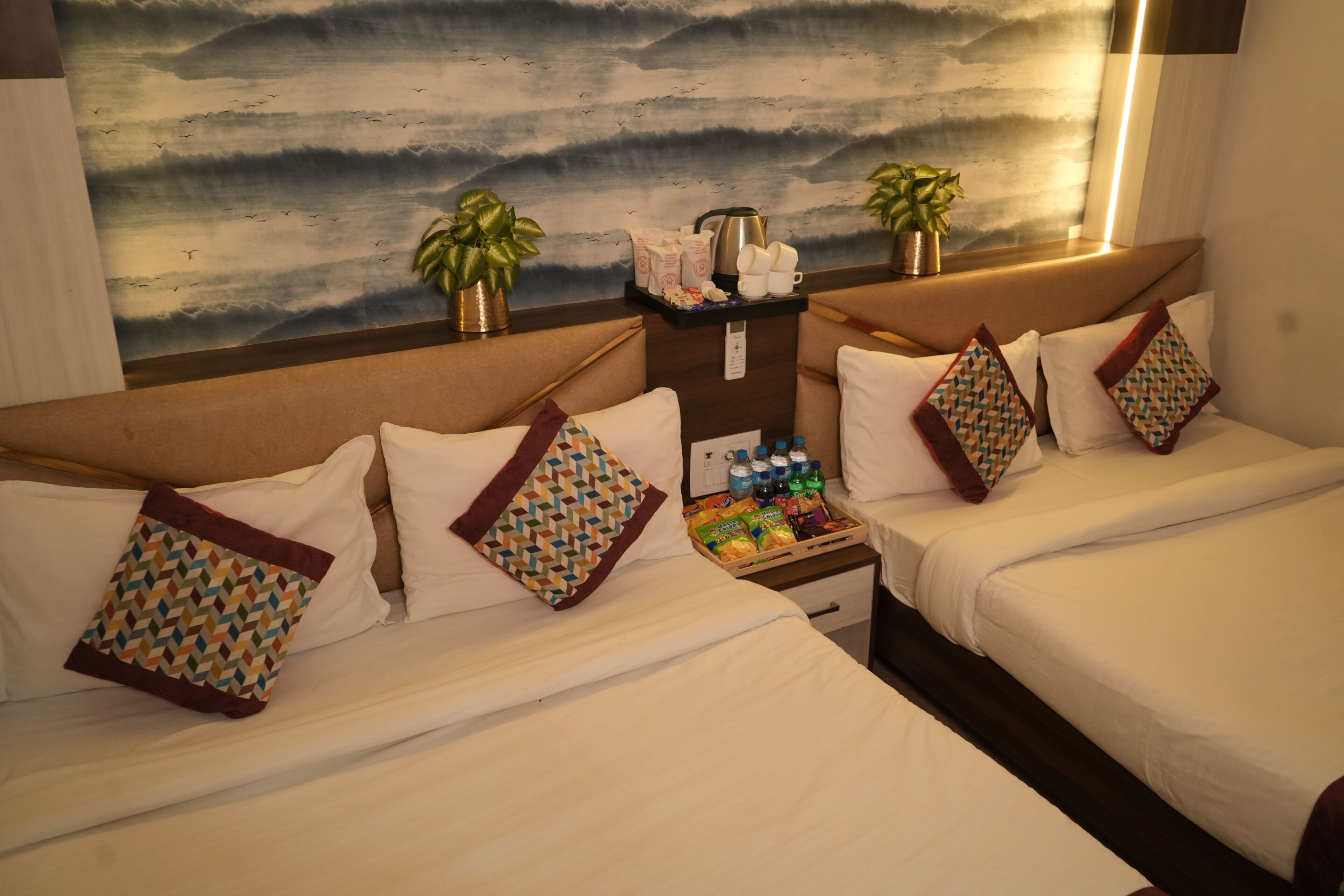 Habitación de hotel con dos camas, una mesita de noche con una bandeja de aperitivos, una cafetera y dos plantas en macetas.