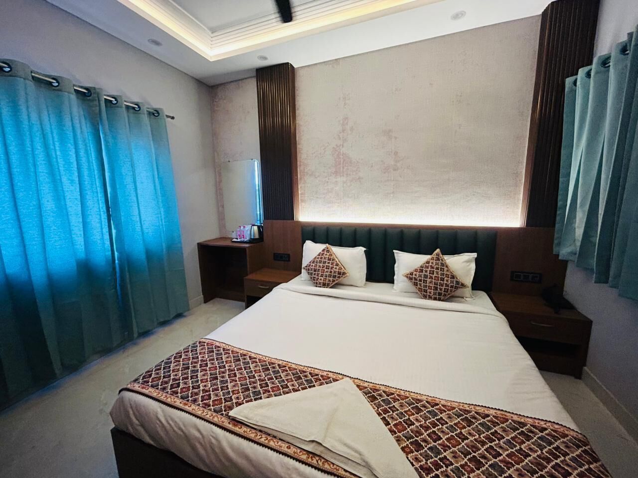 A hotel room with a large bed, two bedside tables, a nightstand, and a window with curtains.