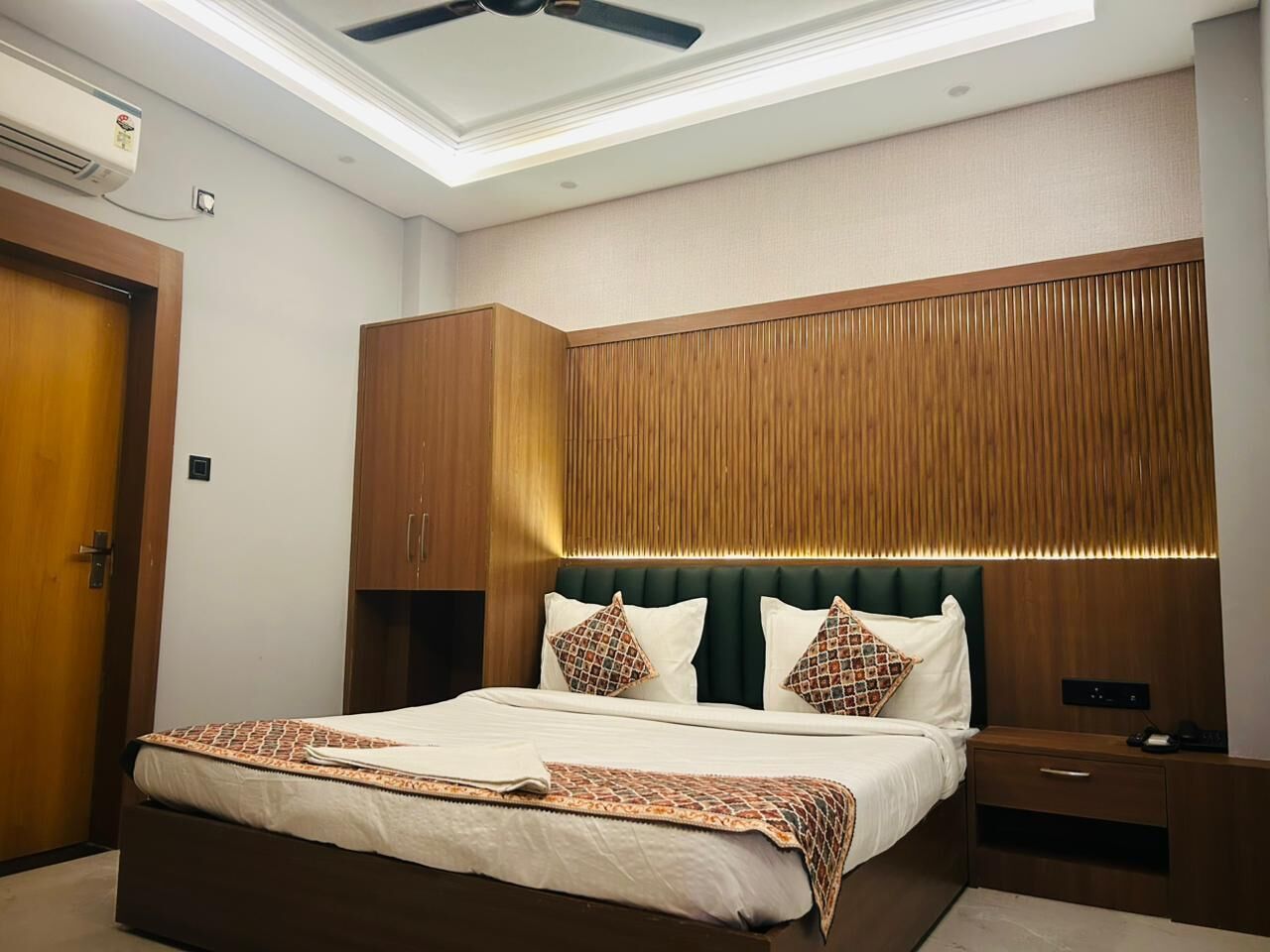 Quarto de hotel bem arrumado, com uma cama grande, cabeceira de madeira e ventoinha no teto.