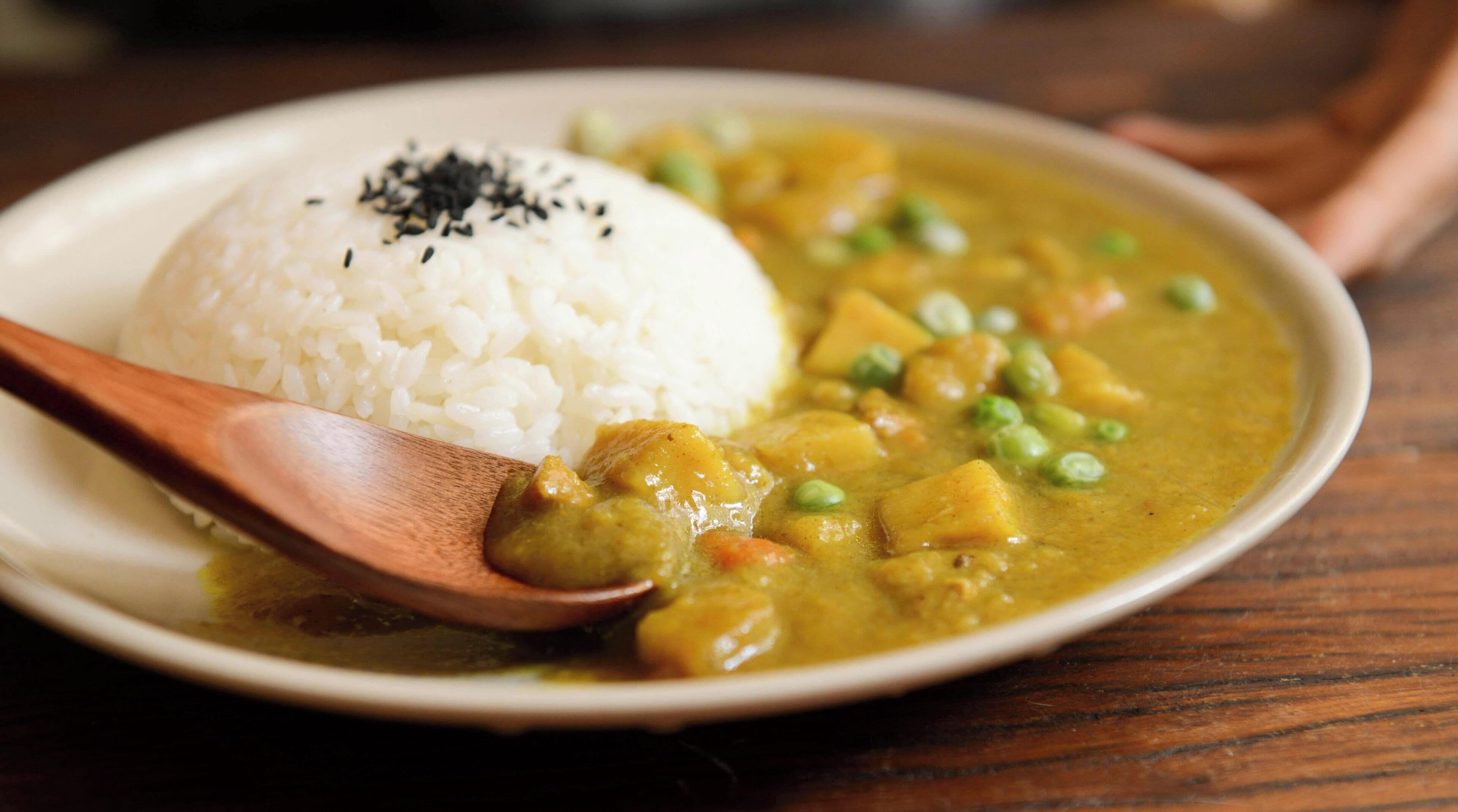 A plate of white rice with a spoon, next to a bowl of curry with peas and potatoes.