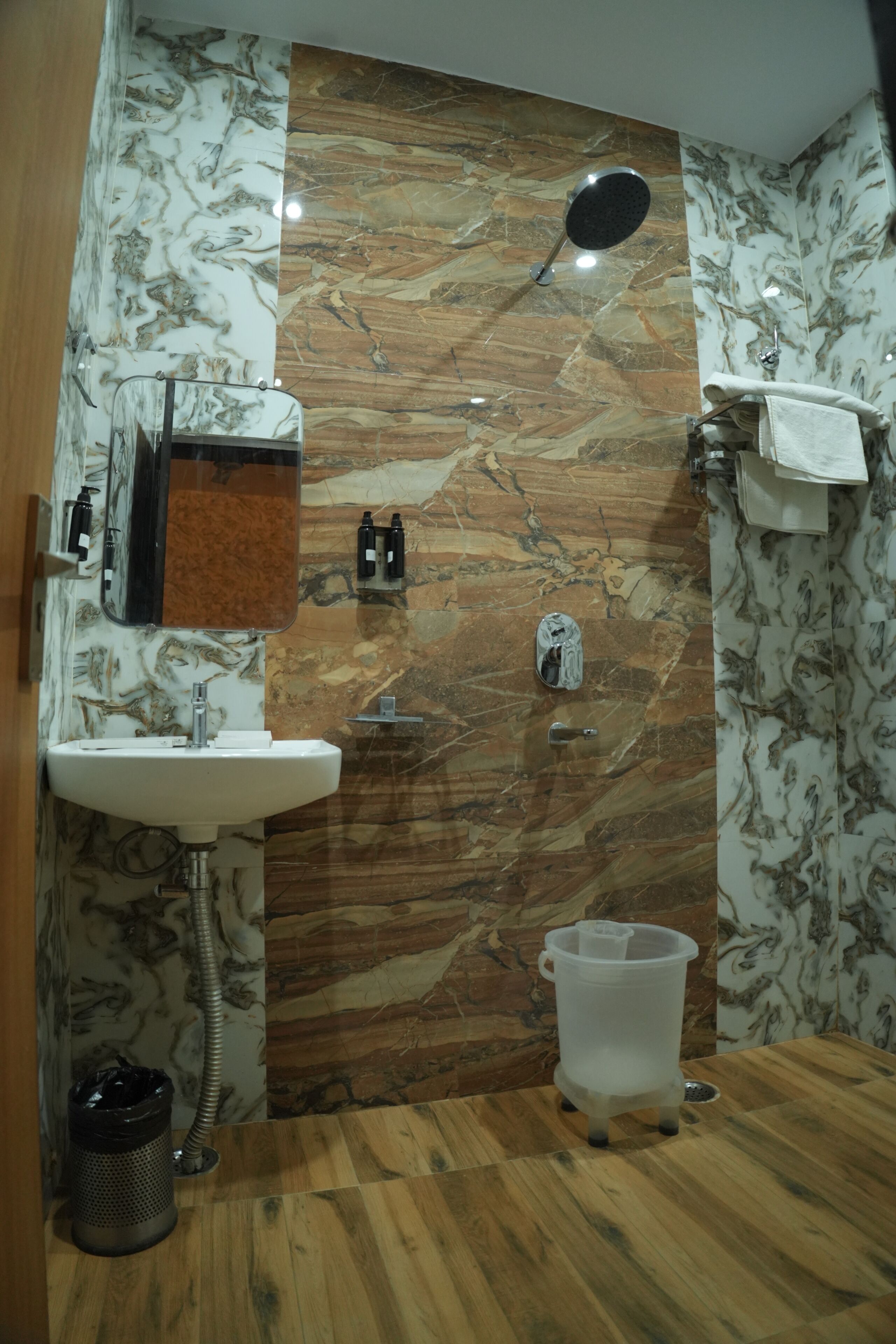 A bathroom with a marble wall, a sink, a shower, and a toilet.
