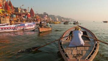 Escena de un río con barcos y un paisaje urbano al fondo.