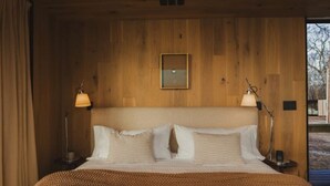 A large bed with a brown blanket, two bedside lamps, a framed picture on the wall, and wooden paneling. - Wilding Hotels Scenic Suite (West Tawakoni)