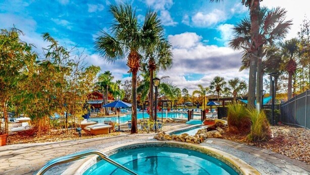 A swimming pool with a curved edge, surrounded by palm trees and lounge chairs. - Spacious, 7R, 4.5BA Pool/Spa Home With Outside Covered Seating Area (166) (Kissimmee)