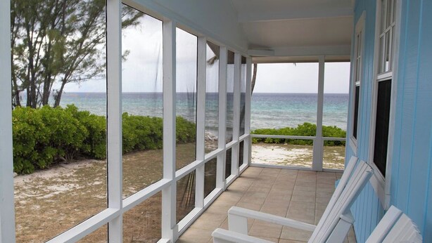 A covered porch with white chairs and a view of the beach and ocean. - Casa Solemare Oceanfront Cottage (Stake Bay)