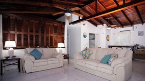 A living room with two beige sofas, a ceiling fan, wooden beams, and a tiled floor. - Casa Solemare Oceanfront Cottage (Stake Bay)