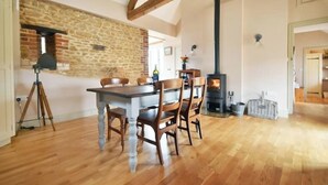 A dining area with a stone wall, wooden beams, a fireplace, and a tripod stand. - The Stone Barn - Luxury Barn in Rural Wiltshire (Studley)