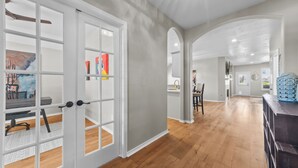 A spacious hallway with a wooden floor, white-framed glass doors, and a kitchen area in the background. - Perfect cottage - Refined Comfort Meets Pet-friendly Backyard Serenity (Tomball)