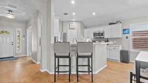 A modern kitchen with white cabinetry, a central island, and a dining area with two chairs. - Perfect cottage - Refined Comfort Meets Pet-friendly Backyard Serenity (Tomball)
