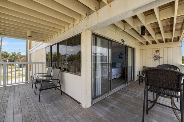 A covered porch with wooden flooring, a sliding glass door leading to a bedroom, and wicker furniture. - Corner Unit ~ King Bed ~ Sunset Views (Cedar Key)