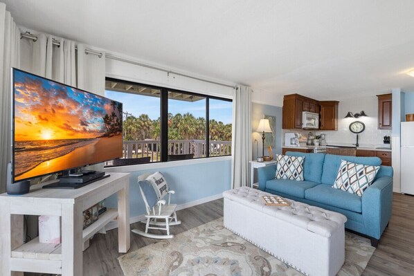 A living room with a TV, a blue sofa, a rocking chair, and a view of the beach.
