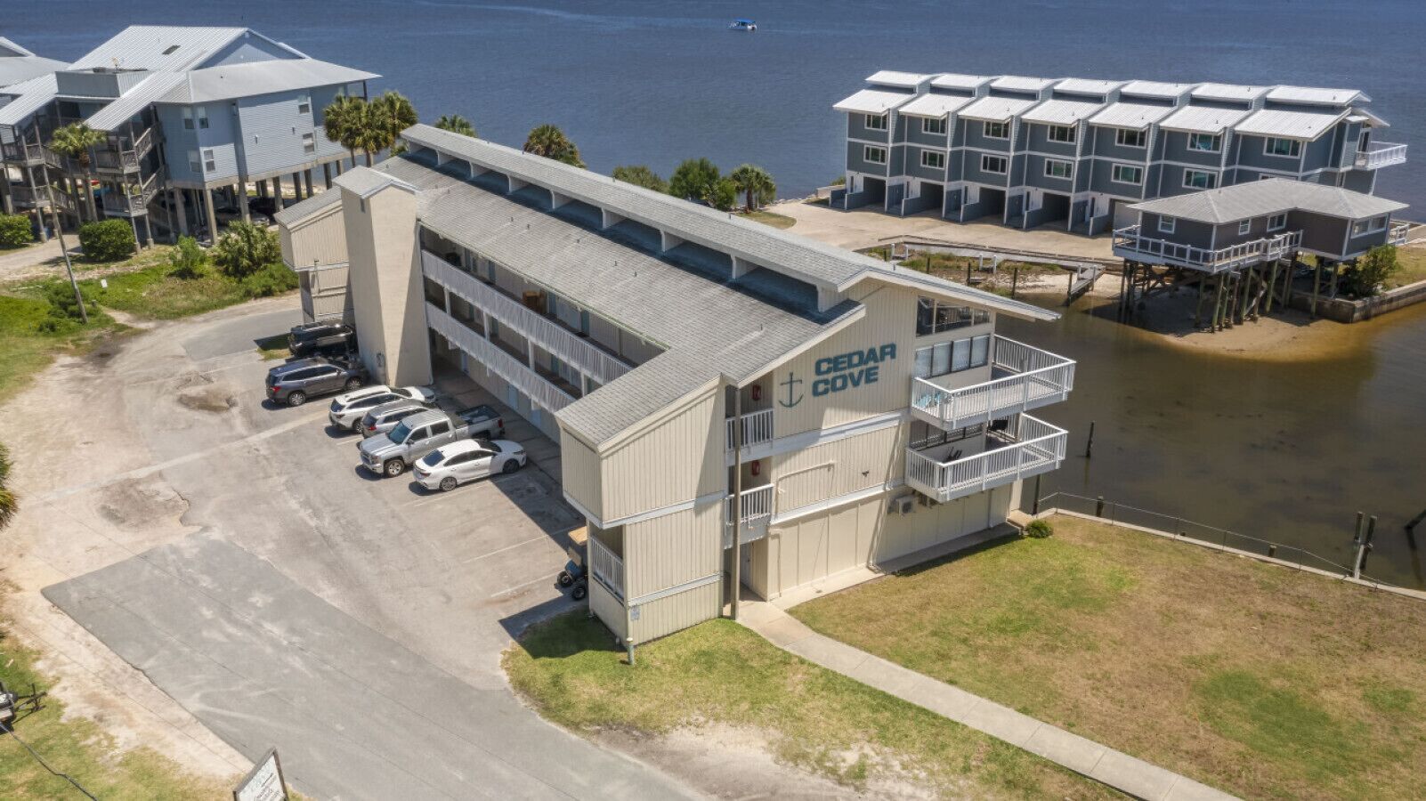 A multi-story hotel with a parking lot, a beach view, and a water body in the background.
