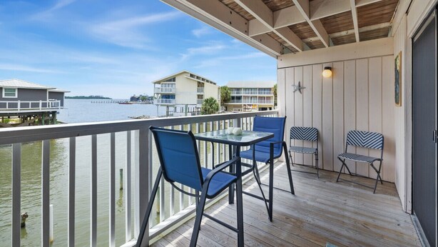 Ein Balkon mit Tisch und Stühlen, der auf ein Gewässer mit Gebäuden im Hintergrund blickt.