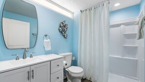 Ein Badezimmer mit weißem Waschtisch, Toilette, Dusche mit weißem Vorhang und einem wandmontierten Spiegel.