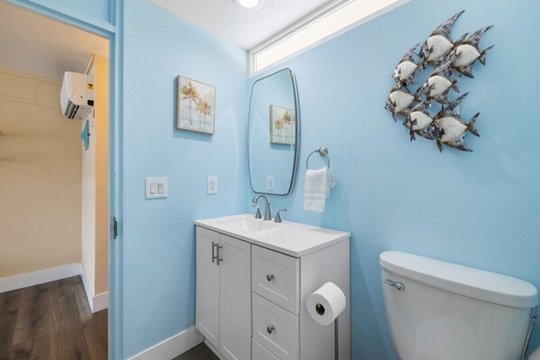 A bathroom with a white sink, a toilet, and a mirror. There are two wall-mounted light switches and a towel hanging on the wall.