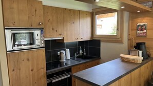 Kompakti keittiö, jossa on puiset kaapit, sisäänrakennettu uuni, mikroaaltouuni, pesuallas ja kahvinkeitin.