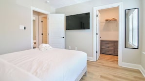 A bedroom with a bed, a TV mounted on the wall, and a walk-in closet. - Steps from the Sand - New 3BR Beach Cottage Near Keesler AFB & Gulf Fun (Biloxi)