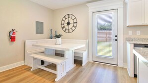 A kitchen with white cabinetry, a double bench at the center, a large wall clock, and a fire extinguisher mounted on the wall. - Steps from the Sand - New 3BR Beach Cottage Near Keesler AFB & Gulf Fun (Biloxi)