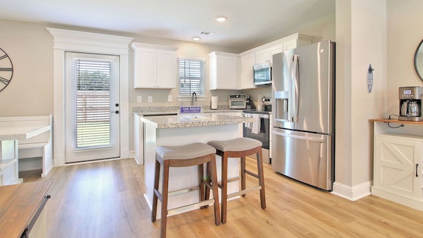 A modern kitchen with white cabinetry, a stainless steel refrigerator, and a coffee maker on the counter. - Steps from the Sand - New 3BR Beach Cottage Near Keesler AFB & Gulf Fun (Biloxi)