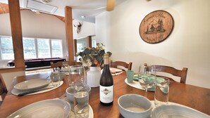 Une table à manger dressée avec des assiettes, des bols, des verres et une bouteille de vin, sous un plafond en bois et avec une assiette décorative accrochée au mur.