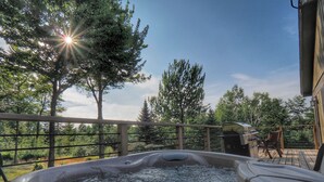 Un bain à remous sur une terrasse en bois, avec vue sur les arbres et un ciel dégagé.