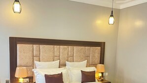 Une chambre d’hôtel avec un grand lit, deux tables de chevet avec des lampes, une tête de lit en bois et un revêtement de sol imitant le marbre.