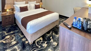 Une chambre d’hôtel avec un grand lit, des lampes de chevet, un bureau avec une télécommande, des bouteilles d’eau et une machine à café.