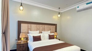 Une chambre d’hôtel avec un grand lit, deux tables de chevet avec des lampes, un luminaire au plafond et un appareil de climatisation.
