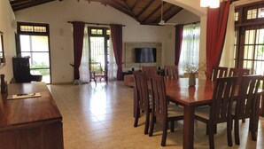 Un vaste espace de vie comprenant une grande table à manger en bois, de nombreuses chaises, un téléviseur à écran plat fixé au mur et un canapé confortable.