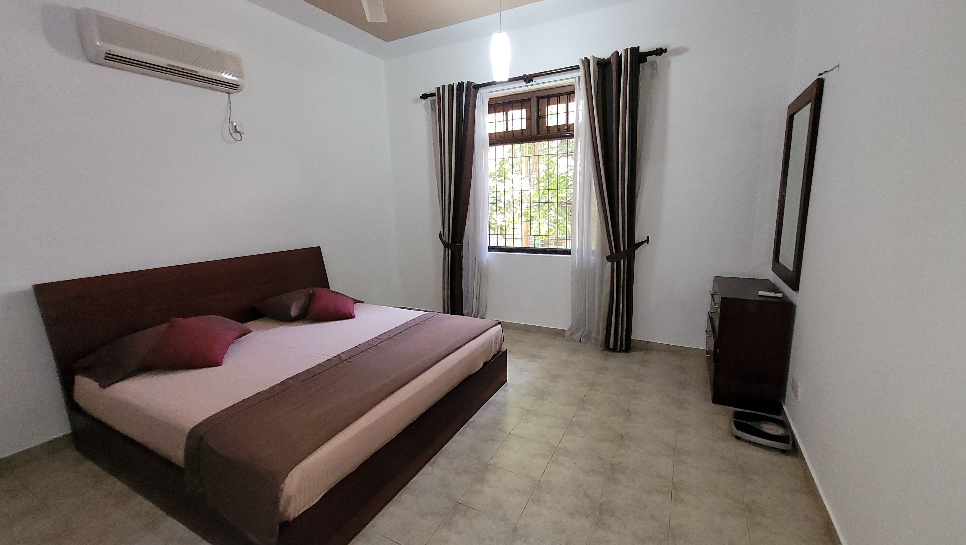 A bedroom with a bed, a small cabinet, and a window with curtains.