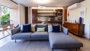 Een moderne woonkamer met een grijze modulaire bank, een houten kast en een keuken met roestvrijstalen apparatuur.