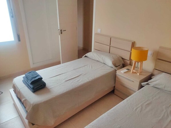 A hotel room with a single bed, a bedside table with a lamp, and a door leading to another room.