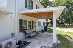 Ein modernes Haus mit einer überdachten Terrasse, Gartenmöbeln und einer Samsung-Klimaanlage.