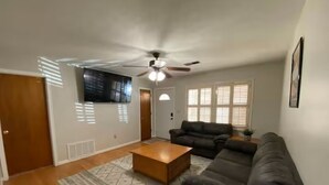 A living room with a ceiling fan, a sectional sofa, a coffee table, and a TV mounted on the wall.