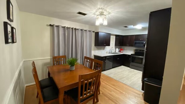 A compact kitchen with dark cabinets, a central island, and a dining area with a wooden table and chairs.