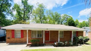 A single-story brick house with a red door and white shutters, a covered front porch, and a well-maintained lawn.