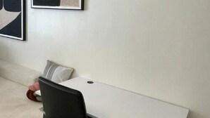 A modern room with a white desk, a black chair, and a beige sofa. There are abstract paintings on the wall. - Cozy 1BR Near Two Rivers & UN | Fast Wi-Fi (Nairobi)