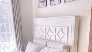 A neatly made bed with a white headboard, a fluffy white rug, and a white nightstand with drawers. - Cozy 1BR Near Two Rivers & UN | Fast Wi-Fi (Nairobi)