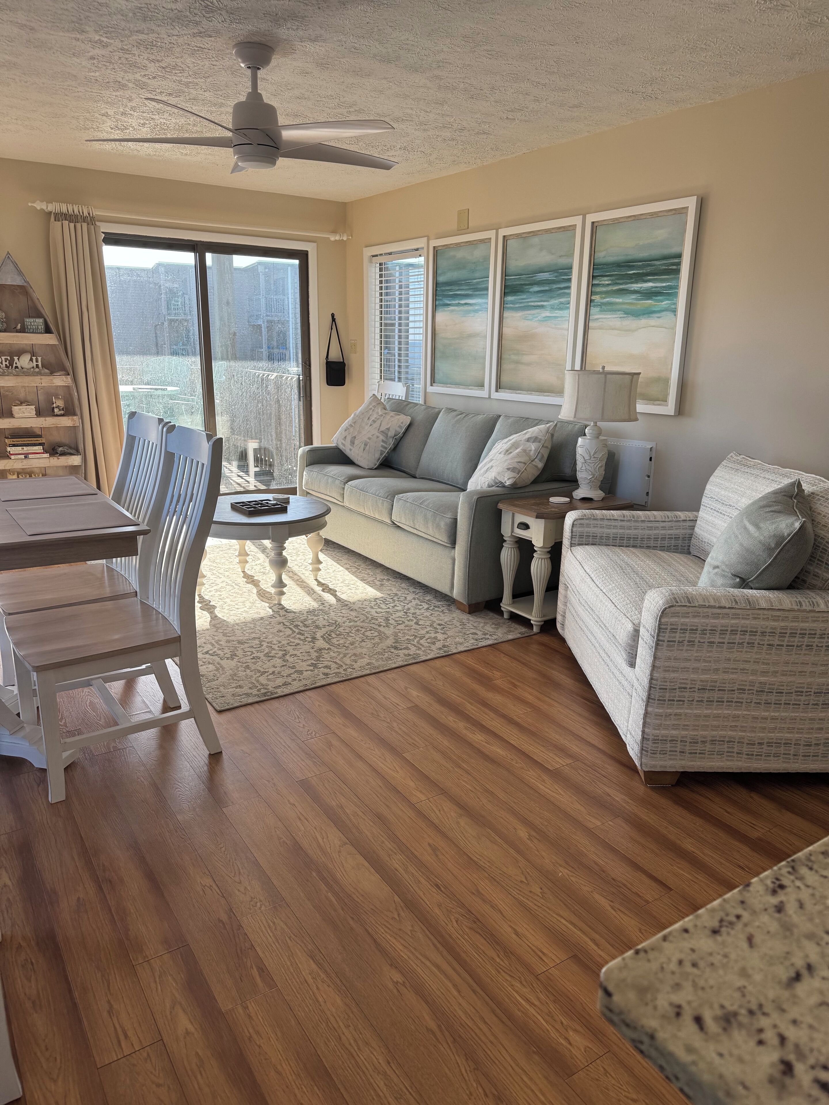 A living room with a wooden floor, a sofa, a dining table with chairs, and a ceiling fan.
