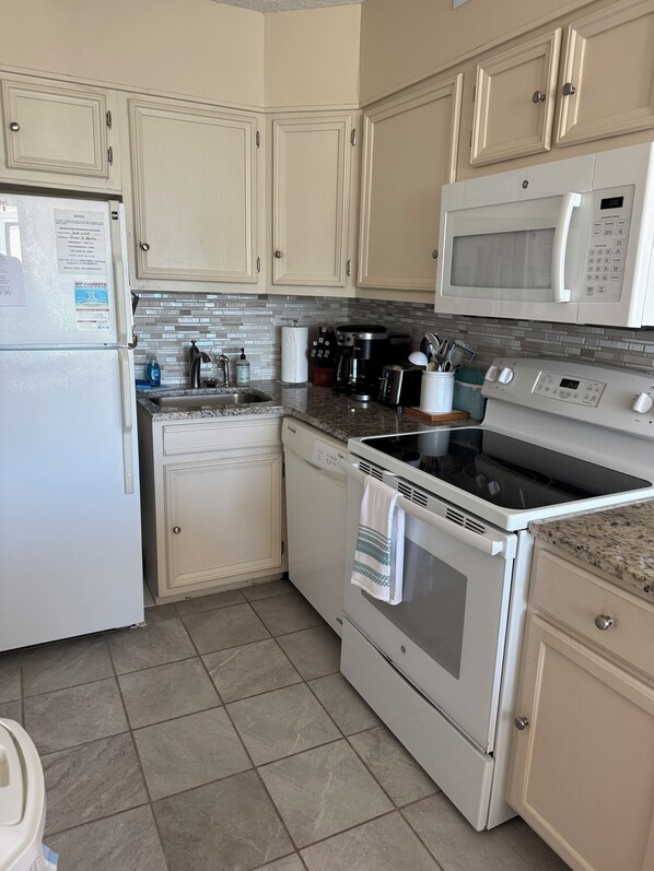 Una cocina con armarios blancos, microondas, estufa y refrigerador.