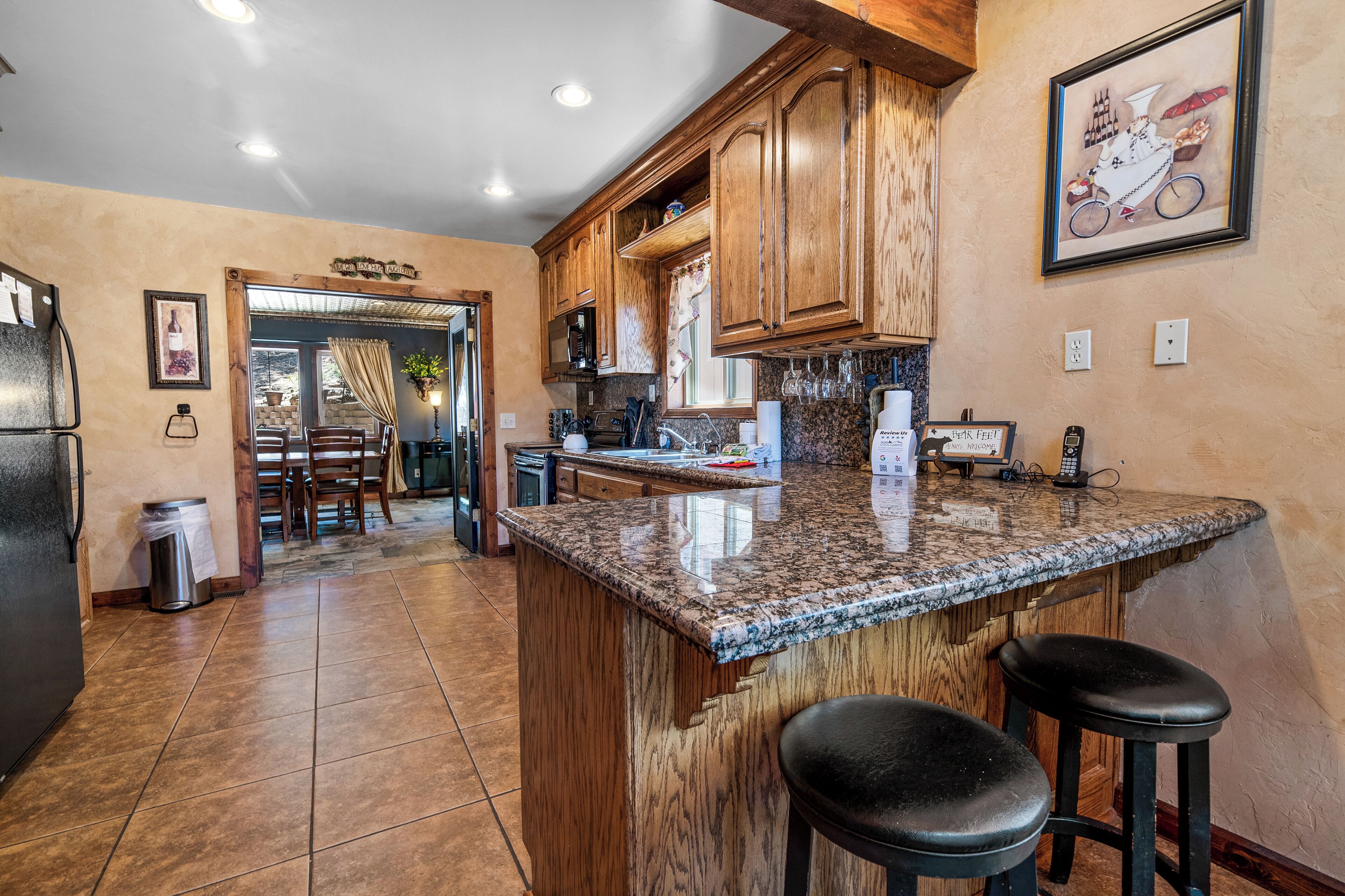 A kitchen with wooden cabinets, granite countertops, and a bar area with stools.