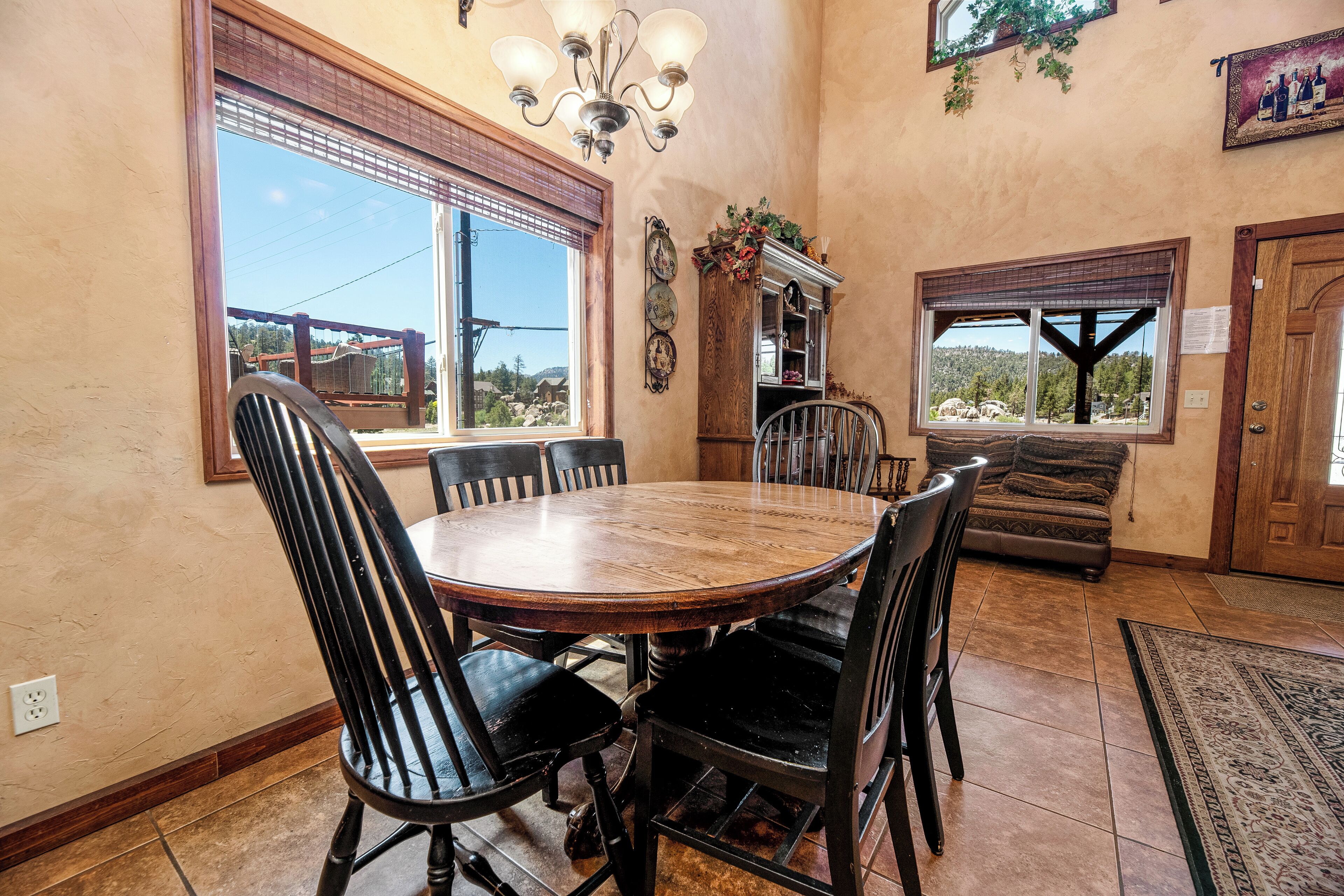 Comedor con una mesa redonda de madera y seis sillas, un candelabro y vistas amplias a través de grandes ventanas.