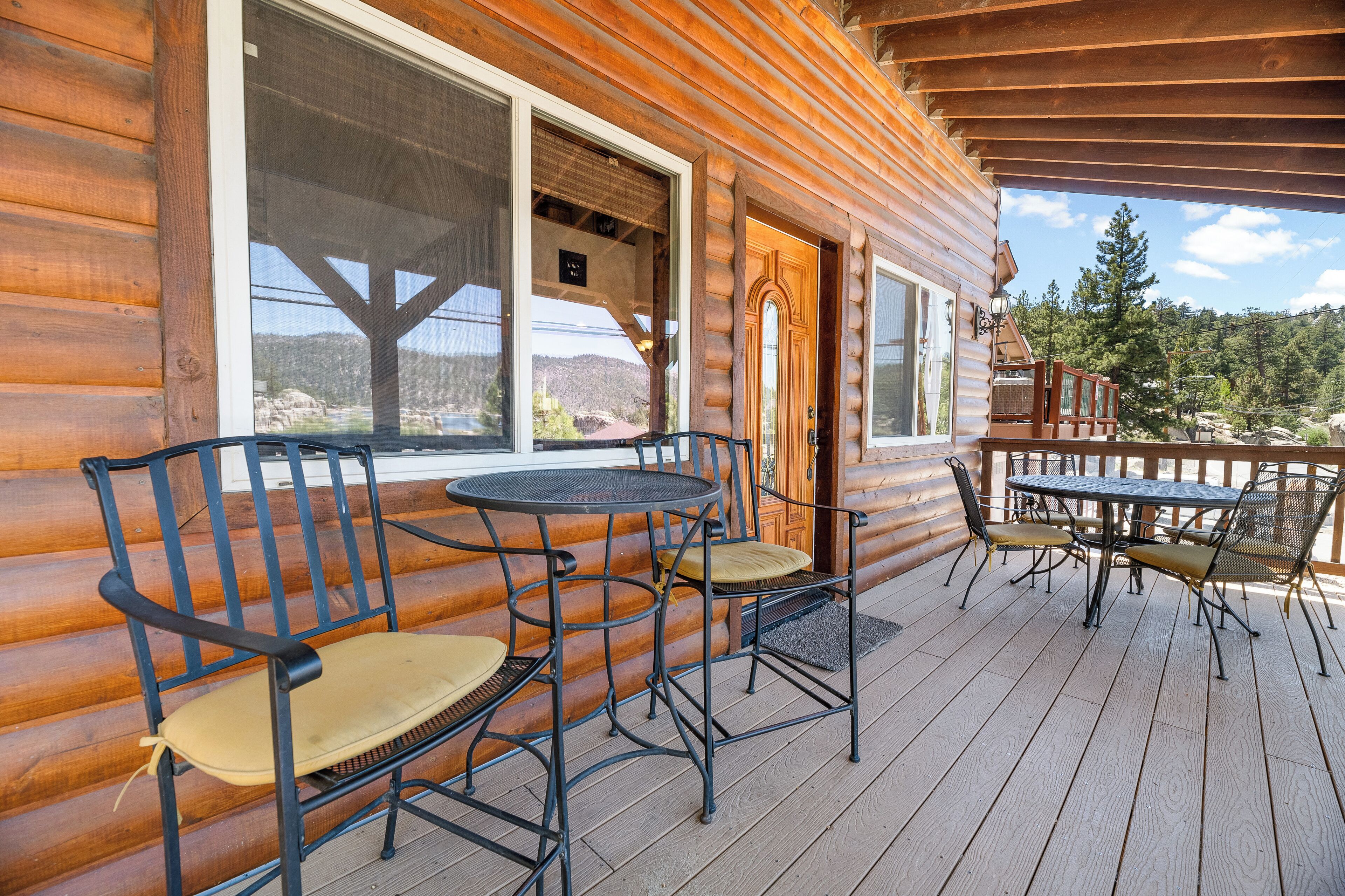 A wooden cabin with a deck featuring outdoor furniture, including chairs and a table.
