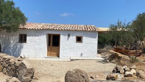 Un pequeño edificio blanco con techo de tejas, puerta de madera y dos ventanas pequeñas.