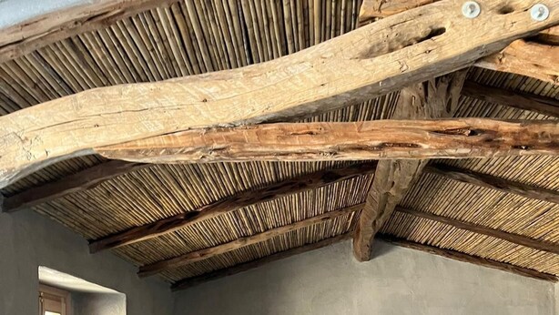 Una habitación rústica con cama, vigas de madera, una ventana y una mesita de noche.