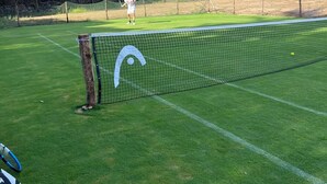 Cancha de tenis con red, rodeada de árboles y un cielo despejado.