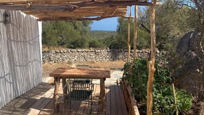 Una terraza de madera con una mesa y sillas, rodeada de un muro de piedra y vegetación.
