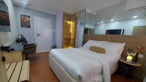 A hotel room with a bed, a desk, a chair, a mirror, and a small table with a lamp.