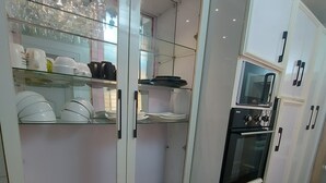 A kitchen with white cabinets, a built-in oven, and a microwave. There are shelves with glassware and plates.