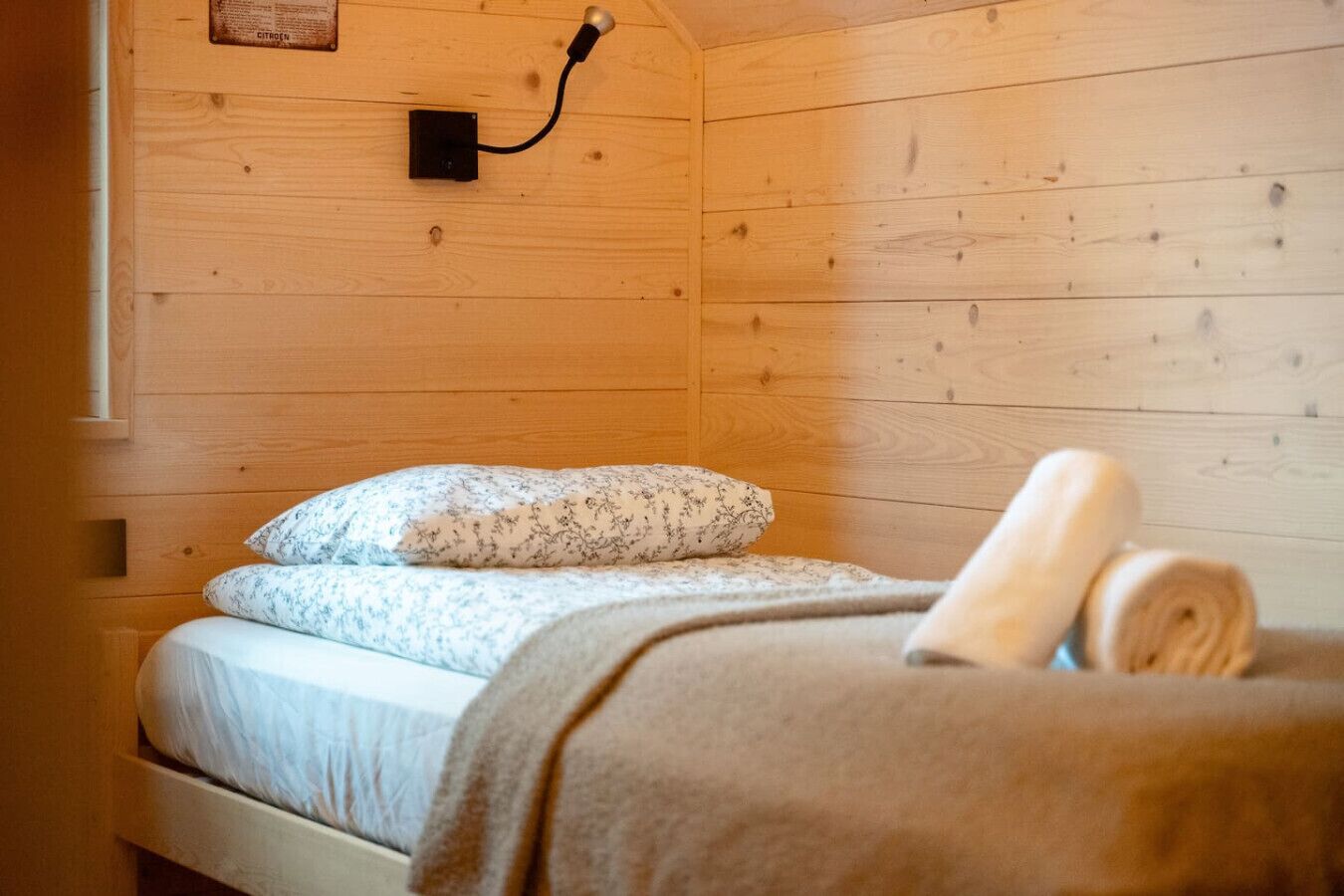 Une pièce de cabane en bois comprenant un lit, une lampe fixée au mur et une fenêtre.